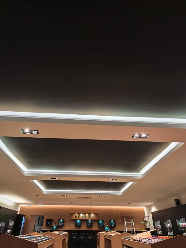 Teto de espaço comercial com luz indireta nas sancas e spots embutidos acesos