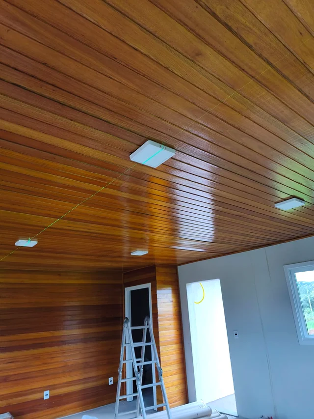 Luminárias em um forro de madeira, com escada de trabalho visível.
