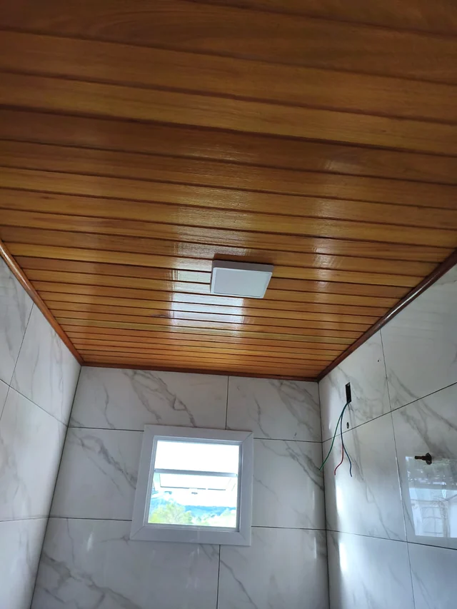 Plafon quadrado instalado no forro de madeira de um banheiro.